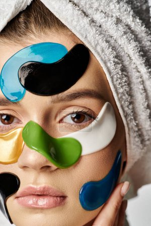 A young woman with a towel wrapped around her head strikes a pose, wearing vivid eye patches.