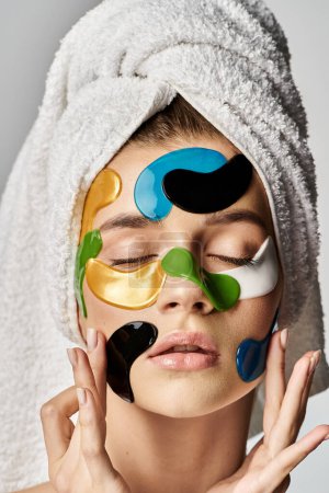 Téléchargez les photos : Une jeune femme sereine avec une serviette sur la tête, les yeux fermés, mettant en valeur les patchs oculaires. - en image libre de droit