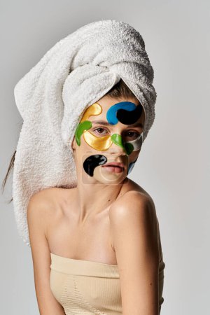 Eine schöne junge Frau, geschmückt mit Augenklappen und Make-up, posiert selbstbewusst mit einem Handtuch, das wie ein Turban um ihren Kopf gewickelt ist.