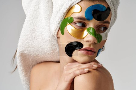 A woman with a towel on her head wears eye patches while embracing self-care with makeup accessories.