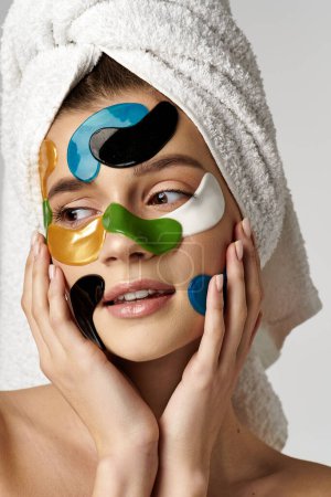 A serene young woman with a towel wrapped around her head and with eye patches on her face.