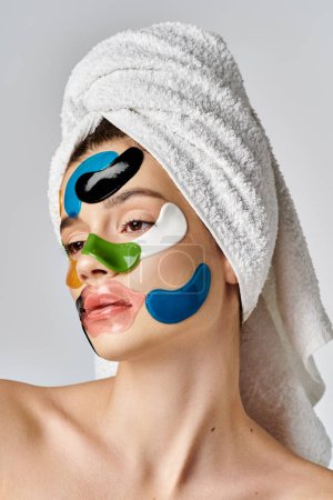 Une jeune femme sereine avec des patchs sur le visage et une serviette enroulée autour de sa tête pose gracieusement.
