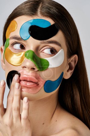 A young woman with eye patches on her face holds her hand up, showcasing bold makeup and artistic expression.