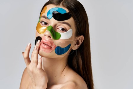 Téléchargez les photos : Une jeune femme avec des patchs sur le visage, présentant un maquillage coloré et créatif avec des couleurs audacieuses et des caractéristiques exagérées. - en image libre de droit