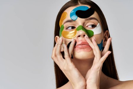 Foto de A young woman with eye patches on her face and hands delicately holds them up to her face in a serene pose. - Imagen libre de derechos