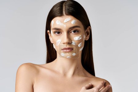 A young woman with striking white cream on her face poses gracefully, embracing her unique beauty.