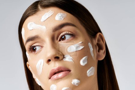 Eine schöne junge Frau mit viel Creme im Gesicht, die ihre Hautpflege-Routine zur Schau stellt.