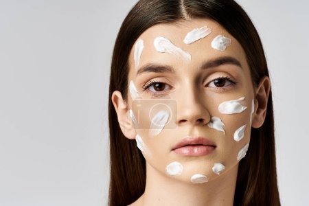 A beautiful young woman poses wearing a white cream on her face, exuding elegance and mystery.