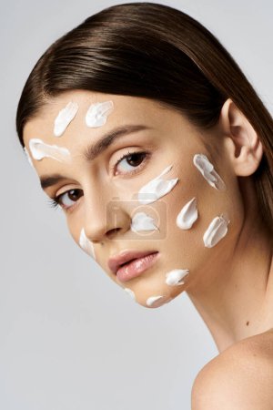 A beautiful young woman with white cream on her face poses in a serene and artistic manner.
