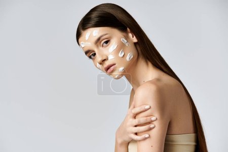 A beautiful young woman poses with white cream on her face, enhancing her natural beauty with cosmetics.