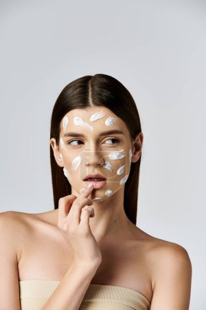 Foto de Una hermosa joven con una crema blanca cubriendo su rostro, exudando misterio y elegancia. - Imagen libre de derechos