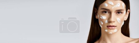 Photo for A young woman posing with a white cream covering her face, enhancing her natural beauty with makeup. - Royalty Free Image