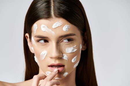 Une jeune femme avec une crème blanche sur le visage, mettant en valeur un mélange de beauté et de mystère.