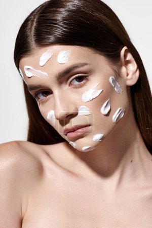 A beautiful young woman posing with white cream on her face, creating a unique and artistic look.