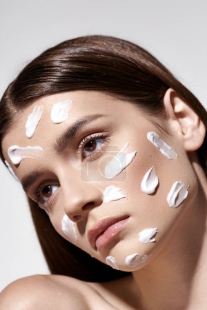 A beautiful young woman with striking white cream on her face, posing artistically.