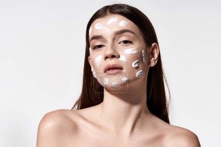 A young woman exudes serenity with white cream on her face, showcasing a unique and artistic makeup design.
