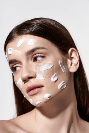 A beautiful young woman poses gracefully with a white cream on her face, exuding an air of mystery and elegance.