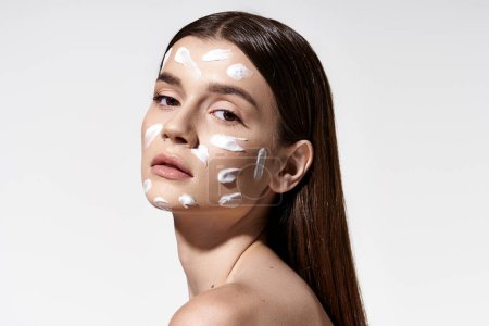 Foto de Una joven emana misterio mientras se pone una crema blanca en la cara, añadiendo un toque de elegancia a su rutina de belleza.. - Imagen libre de derechos