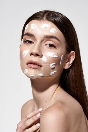 A beautiful young woman elegantly showcases a white cream on her face, adding an air of mystery and allure.