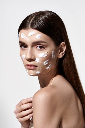 Eine schöne junge Frau posiert mit ätherischer weißer Creme auf ihrem Gesicht und zeigt einzigartige und künstlerische Make-up-Techniken.