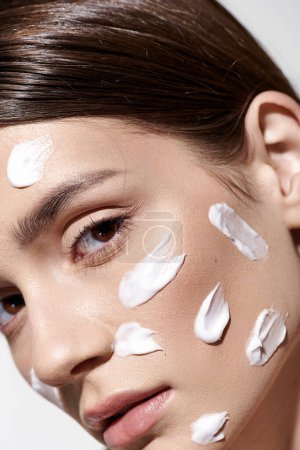 Une belle jeune femme avec une généreuse quantité de crème sur le visage, prenant un moment pour prendre soin de sa peau avec soin.