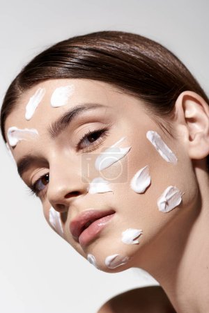 Eine Frau mit viel weißer Creme im Gesicht, die sich einer Hautbehandlung oder Make-up-Anwendung unterzieht und gelassen wirkt.