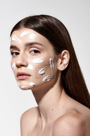 A striking young woman wearing a white cream, enhancing her exquisite features with makeup and facial treatments.