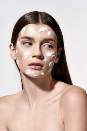 A woman with a white cream on her face, showcasing a blend of beauty and mystery with strategic makeup application.