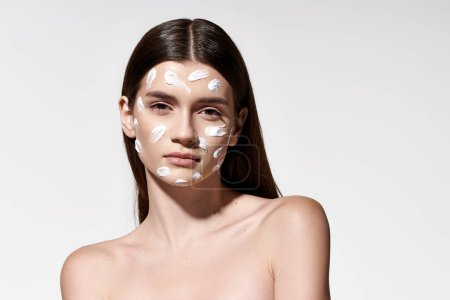 Téléchargez les photos : A beautiful young woman gracefully wears a white cream on her face, exuding mystery and elegance. - en image libre de droit