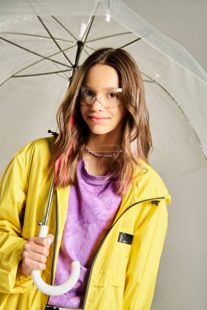 A stylish teenage girl in a yellow jacket energetically holds an umbrella under the rain.