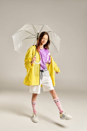 Ein stilvolles Teenager-Mädchen in einem gelben Regenmantel hält freudig einen Regenschirm in der Hand, der lebendige Energie und Positivität ausstrahlt..