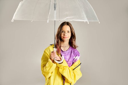 Una adolescente de moda, vestida con un vibrante impermeable amarillo, posa enérgicamente con un paraguas en un día lluvioso.