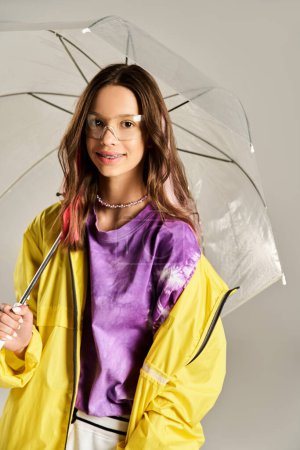 A stylish teenage girl in a vibrant yellow jacket strikes a pose, holding a colorful umbrella.