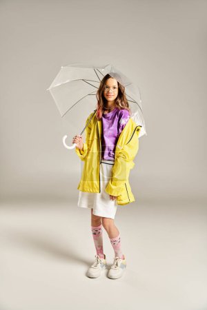 Teenage girl striking a pose in a stylish yellow raincoat, holding a colorful umbrella.