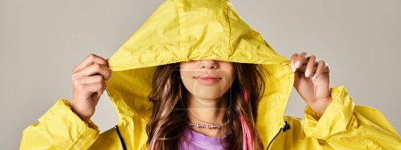 Ein stilvolles Teenager-Mädchen in einem gelben Regenmantel, das ihr Gesicht mit den Händen bedeckt.