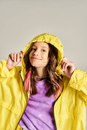 Une adolescente élégante pose activement dans un imperméable jaune vif, exsudant vivacité et énergie par une journée ensoleillée.