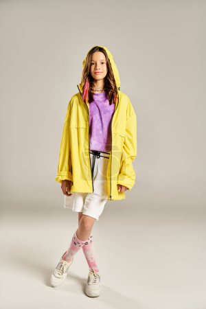 Ein modisches Teenager-Mädchen posiert in einem leuchtend gelben Regenmantel, der Stil und Energie ausstrahlt.