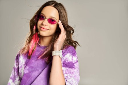 Stilvolles Teenie-Mädchen posiert selbstbewusst in rosa Haaren und lila Hemd und setzt trendige Sonnenbrillen auf.