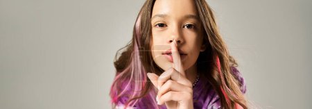 Ein stilvolles Teenager-Mädchen mit langen Haaren hält ihren Finger in einer geheimnisvollen Geste an die Lippen.