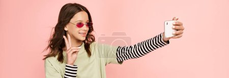 Foto de Una adolescente de moda en traje vibrante tomando una selfie con su teléfono celular. - Imagen libre de derechos