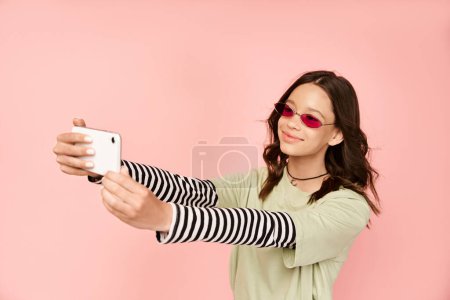 Ein modisches Teenager-Mädchen in lebendiger Kleidung und Sonnenbrille macht ein Selfie mit einem Handy.