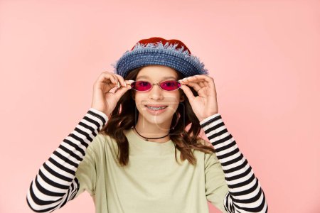 A stylish teenage girl strikes a pose in vibrant attire, wearing sunglasses and a hat.
