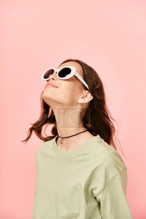 Téléchargez les photos : Une jeune femme à la mode en tenue vibrante, portant des lunettes de soleil, lève les yeux vers le ciel. - en image libre de droit