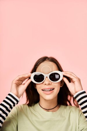 Foto de Una adolescente con estilo posa con confianza en una camisa verde vibrante y gafas de sol blancas de moda. - Imagen libre de derechos
