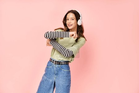 Téléchargez les photos : Une adolescente élégante en tenue vibrante portant un jean et un casque, frappant une pose. - en image libre de droit
