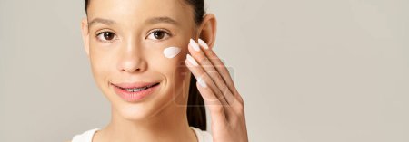 A stylish teenage girl with vibrant attire applies cream on her face for a healthy, glowing complexion.