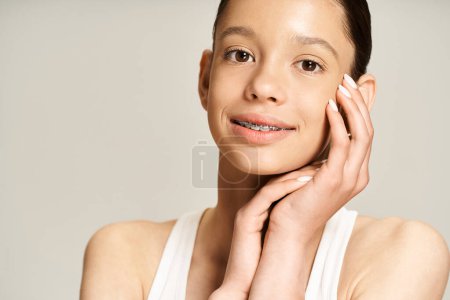 A stylish teenage girl in vibrant attire poses with hands on face in an active and engaging manner.
