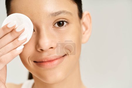 Ein stilvolles Teenager-Mädchen, elegant gekleidet, reinigt zart ihr Gesicht mit einem Wattepad.