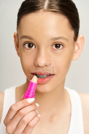 Ein stilvolles, gut aussehendes Teenie-Mädchen in lebendiger Kleidung trägt leidenschaftlich rosa Lippenstift auf ihre Lippen auf und unterstreicht ihre Schönheit.