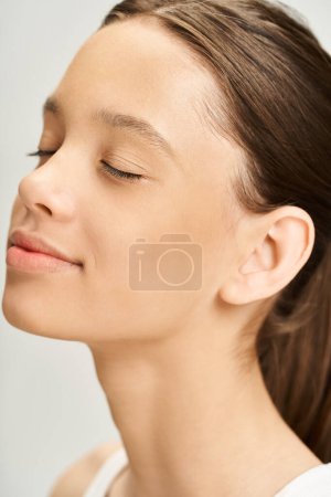 A stylish young woman with her eyes closed and long hair in a ponytail, exudes a sense of calm and elegance.